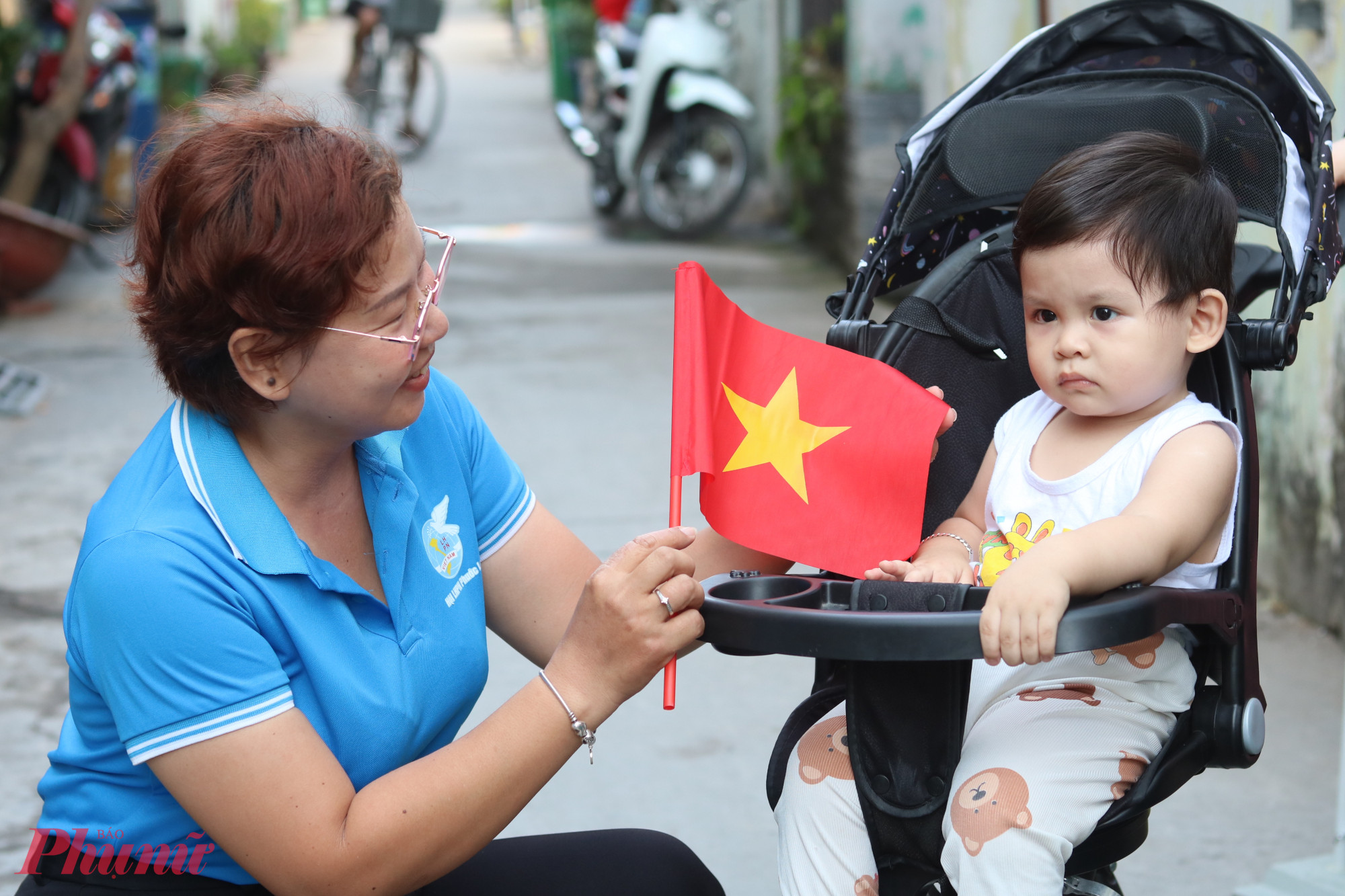 B&ecirc;n cạnh đổi cờ mới cho c&aacute;c hộ d&acirc;n, Hội LHPN phường Phước Long B c&ograve;n tặng cờ cầm tay để b&agrave; con tham gia c&aacute;c hoạt động kỷ niệm 50 năm Ng&agrave;y Giải ph&oacute;ng miền Nam thống nhất đất nước (30/4/1975 &ndash; 30/4/2025). Trong ảnh, c&aacute;c em nhỏ được phụ huynh đưa đi nhận cờ. 