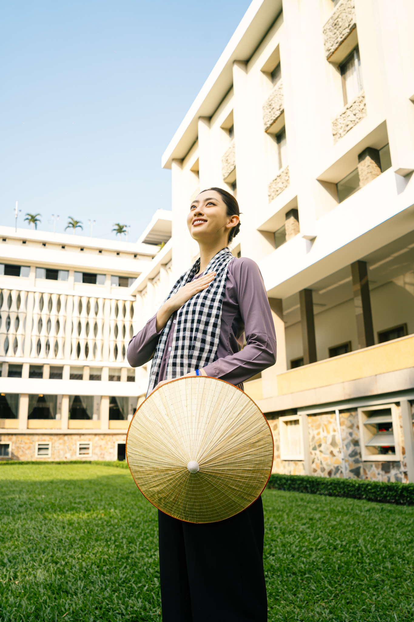 Hoa hậu Lương Thuỳ Linh diện &aacute;o d&agrave;i trắng v&agrave; &aacute;o b&agrave; ba nam bộ chụp ảnh trong khu&ocirc;n vi&ecirc;n Hội trường Thống Nhất (Dinh Độc Lập). 