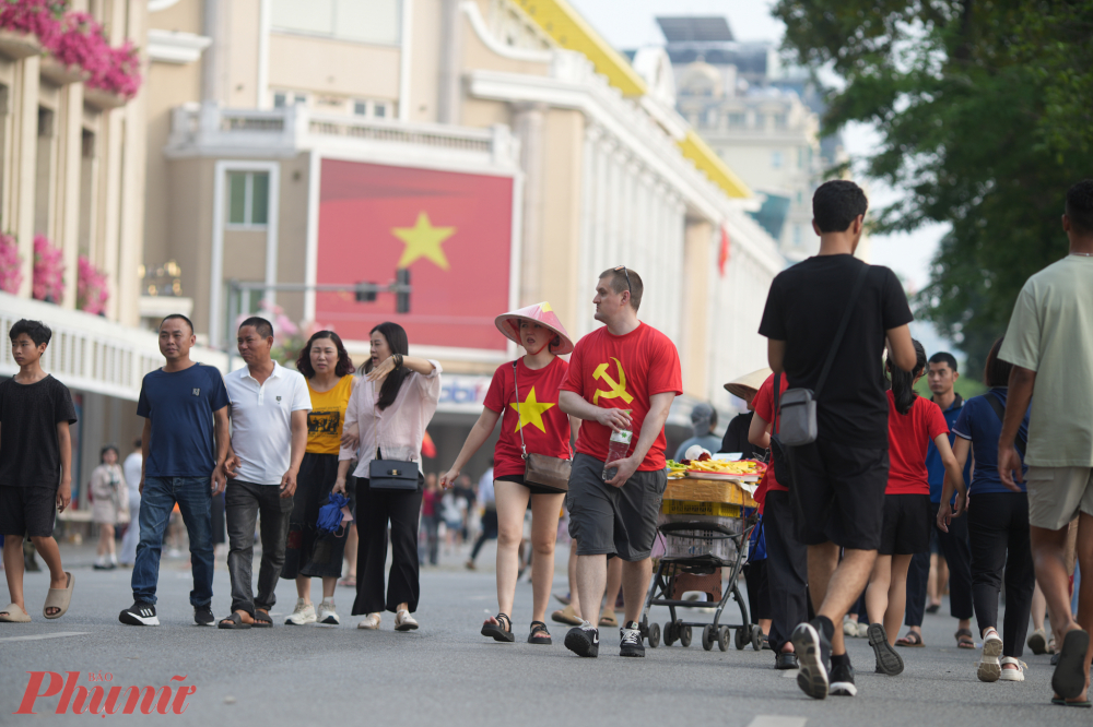 Những du kh&aacute;ch nước ngo&agrave;i th&iacute;ch th&uacute; mặc tr&ecirc;n m&igrave;nh m&agrave;u &aacute;o cờ đỏ sao v&agrave;ng, cờ Đảng b&uacute;a liềm, đội n&oacute;n l&aacute; đi dạo tr&ecirc;n phố đi bộ.