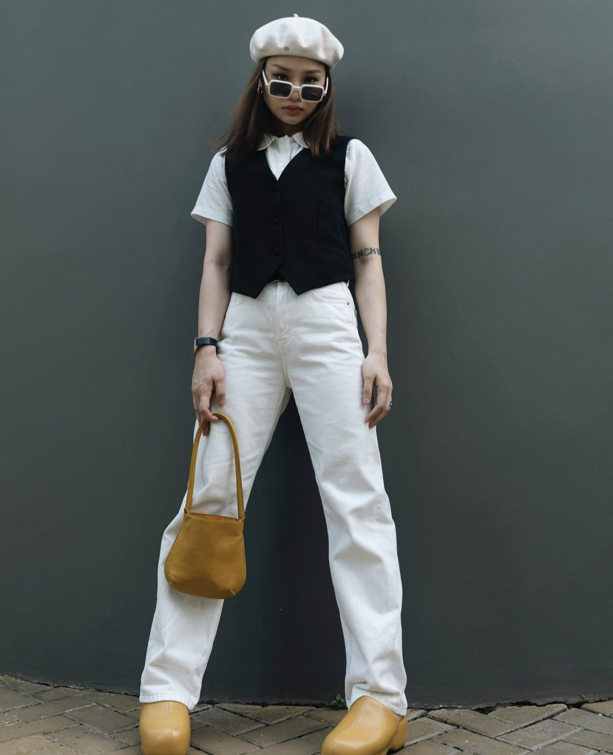gu thời trang ph&oacute;ng kho&aacute;ng pha ch&uacute;t cổ điển. C&ocirc; phối sơ mi trắng v&agrave; &aacute;o gile đen c&ugrave;ng quần jeans trắng, tạo n&ecirc;n tổng thể tối giản nhưng nổi bật. Mũ beret, t&uacute;i x&aacute;ch v&agrave; gi&agrave;y v&agrave;ng m&ugrave; tạt l&agrave; điểm nhấn th&uacute; vị, mang lại sắc m&agrave;u trẻ trung, c&aacute; t&iacute;nh v&agrave; đậm chất nghệ sĩ đường phố.