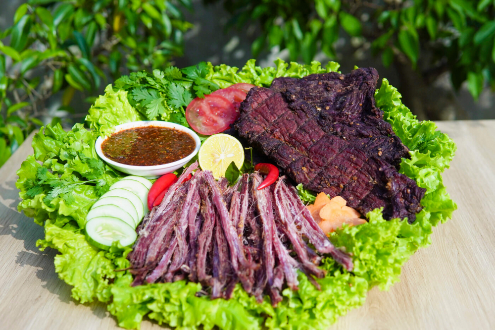 Thịt tr&acirc;u g&aacute;c bếp l&agrave; đặc sản nổi tiếng của v&ugrave;ng n&uacute;i T&acirc;y Bắc, đặc biệt được đồng b&agrave;o Th&aacute;i v&agrave; M&ocirc;ng ưa chuộng. Thịt tr&acirc;u tươi, thường l&agrave; phần bắp, được th&aacute;i dọc thớ, ướp với mắc kh&eacute;n, hạt dổi, ớt, gừng v&agrave; nhiều gia vị n&uacute;i rừng, rồi treo l&ecirc;n g&aacute;c bếp hun kh&oacute;i từ củi thơm. Nhờ c&aacute;ch l&agrave;m n&agrave;y, thịt vừa kh&ocirc;, vừa thấm đậm gia vị, lại giữ được vị ngọt đặc trưng. Khi ăn, chỉ cần nướng lại hoặc hấp cho mềm, x&eacute; từng sợi chấm với chẩm ch&eacute;o l&agrave; đ&atilde; cảm nhận trọn hương vị cay, thơm, mặn m&agrave; của n&uacute;i rừng T&acirc;y Bắc.        Hỏi ChatGPT