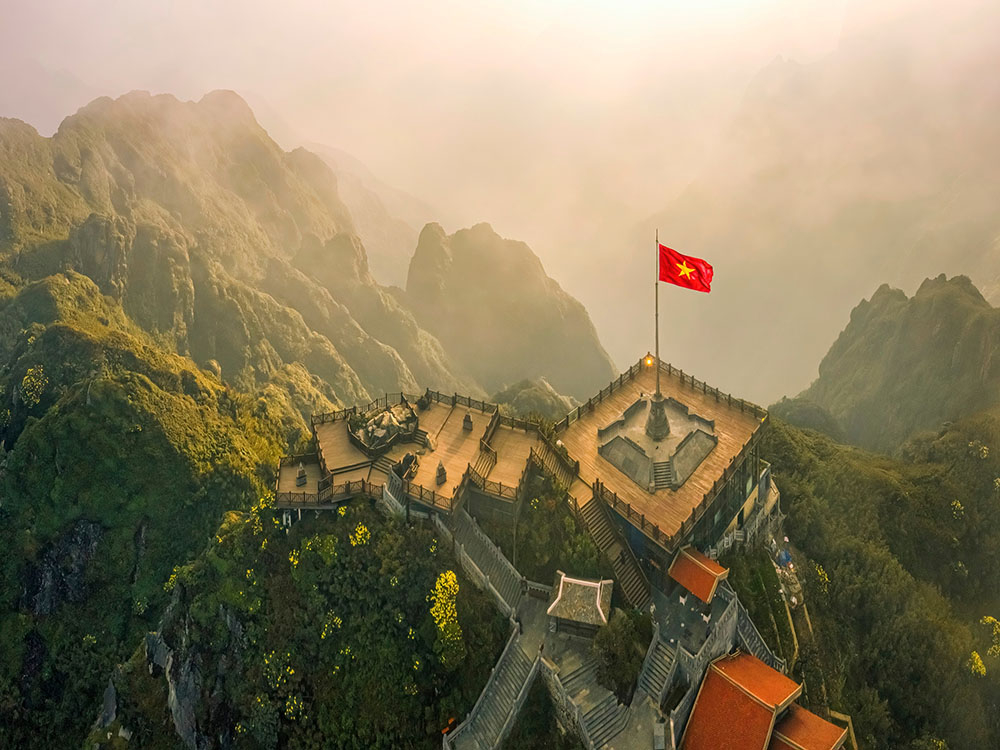 Chinh phục đỉnh Fansipan &ndash; ngọn n&uacute;i cao nhất Việt Nam với độ cao 3.147,3 m&eacute;t &ndash; từ l&acirc;u đ&atilde; trở th&agrave;nh &ldquo;huy hiệu&rdquo; danh dự của d&acirc;n phượt ba l&ocirc;. Đứng tr&ecirc;n đỉnh, ph&oacute;ng tầm mắt ra biển m&acirc;y bồng bềnh c&ugrave;ng những d&atilde;y n&uacute;i đ&aacute; gồ ghề k&eacute;o d&agrave;i bất tận, du kh&aacute;ch kh&ocirc;ng khỏi cho&aacute;ng ngợp trước vẻ đẹp h&ugrave;ng vĩ. H&agrave;nh tr&igrave;nh chinh phục c&oacute; thể g&oacute;i gọn trong một ng&agrave;y, với những bước ch&acirc;n lấm b&ugrave;n xuy&ecirc;n qua rừng rậm, leo dốc trơn trượt v&agrave; lối m&ograve;n rễ c&acirc;y chằng chịt; hoặc thong thả hơn khi dừng lại cắm trại tr&ecirc;n sườn n&uacute;i để tận hưởng thi&ecirc;n nhi&ecirc;n. D&ugrave; chọn c&aacute;ch n&agrave;o, đ&oacute; cũng l&agrave; một thử th&aacute;ch đ&ograve;i hỏi sức bền. Ng&agrave;y nay, du kh&aacute;ch c&ograve;n c&oacute; thể dễ d&agrave;ng &ldquo;chạm m&acirc;y&rdquo; chỉ trong 15 ph&uacute;t nhờ tuyến c&aacute;p treo hiện đại &ndash; lựa chọn ho&agrave;n hảo cho những ai muốn chi&ecirc;m ngưỡng cảnh sắc ngoạn mục m&agrave; kh&ocirc;ng cần đổ nhiều mồ h&ocirc;i - Ảnh: Wanderlust