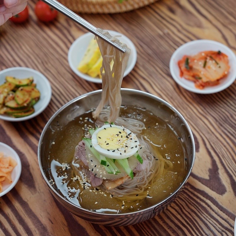 Kh&ocirc;ng giống c&aacute;c m&oacute;n nước n&oacute;ng truyền thống, m&igrave; lạnh mang lại cảm gi&aacute;c m&aacute;t từ vị gi&aacute;c đến cơ thể. Nước d&ugrave;ng thường được l&agrave;m từ nước xương hoặc nước kim chi, ướp lạnh s&acirc;u, đ&ocirc;i khi c&ograve;n c&oacute; đ&aacute; vi&ecirc;n. Khi ăn, thực kh&aacute;ch trộn đều với m&igrave;, thịt b&ograve;, trứng, dưa leo v&agrave; kim chi, tạo n&ecirc;n tổng thể vừa thanh vừa đậm đ&agrave;. Tại S&agrave;i G&ograve;n, m&oacute;n ăn n&agrave;y ng&agrave;y c&agrave;ng phổ biến, đặc biệt trong c&aacute;c qu&aacute;n H&agrave;n Quốc. Nhiều thực kh&aacute;ch cho biết chỉ cần một t&ocirc; m&igrave; lạnh l&agrave; đủ 'hạ nhiệt' ngay giữa trưa nắng, bởi vị lạnh dịu v&agrave; dễ ti&ecirc;u h&oacute;a hơn c&aacute;c m&oacute;n n&oacute;ng. Gi&aacute; từ 50.000-100.000 đồng -Ảnh: Canva