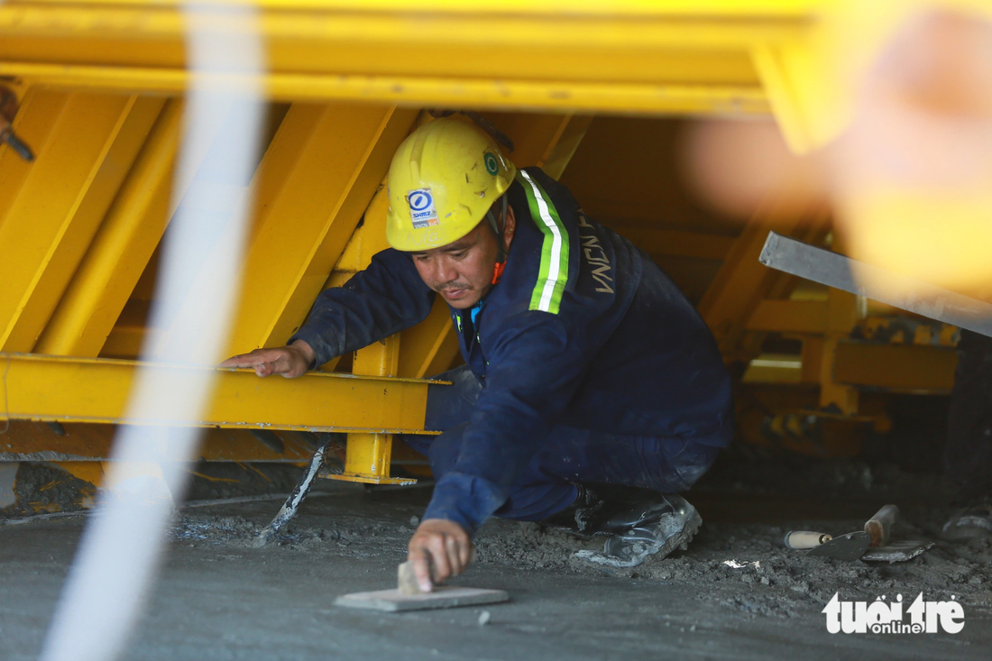 Một công nhân làm phẳng bê tông trong hộc đúc. Sau khi tái khởi động, việc thi công diễn ra hối hả để tiến độ dự án được đáp ứng. Nhiều năm vắng bóng công nhân, nay công trường đã hồi sinh trở lại. Tiếng máy móc, phân công công việc rôm rả một góc sông Soài Rạp