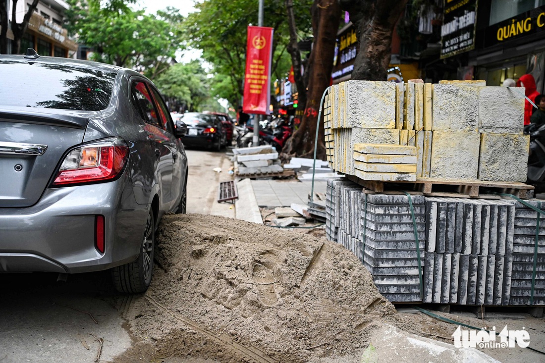 Chiếc ô tô kẹt trong đống cát tập kết ngay dưới lòng đường - Ảnh: HỒNG QUANG