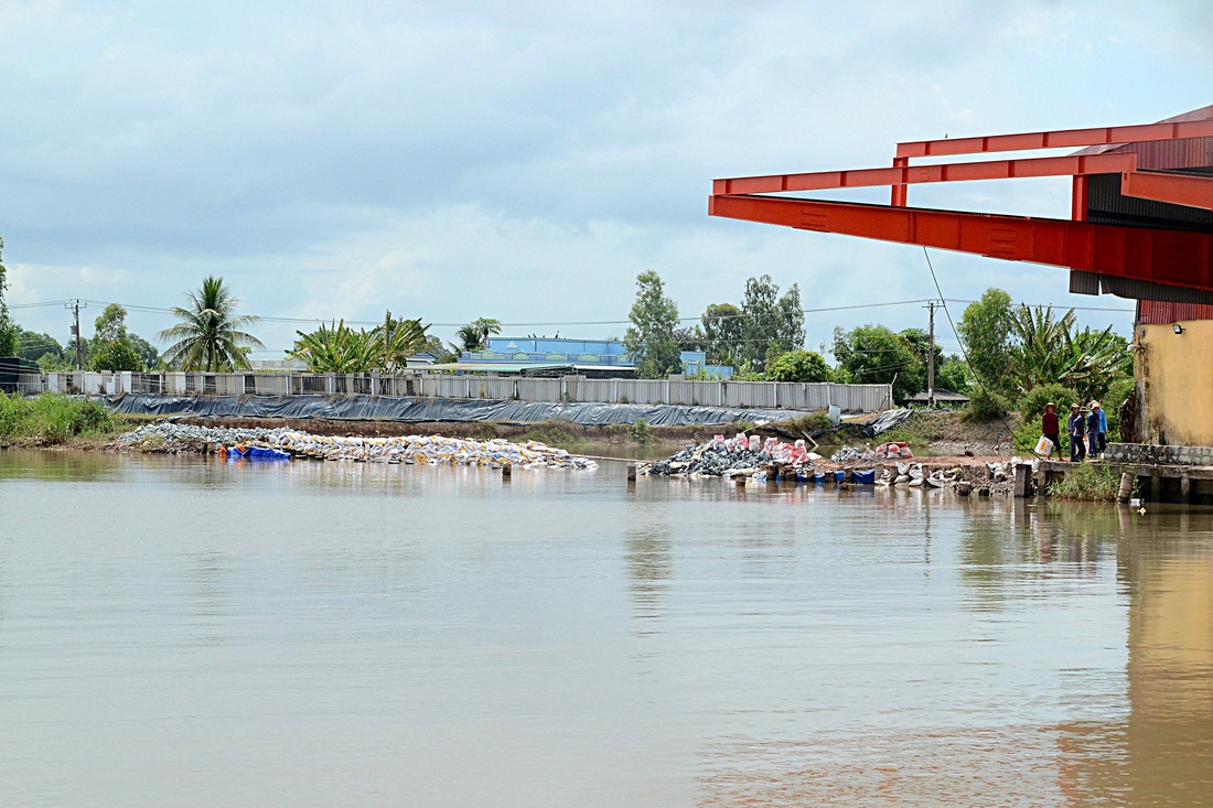 Tại bến phà Tân Long ban quản lý và người dân gia cố bờ sông bằng đá và bao cát để phòng sạt lở