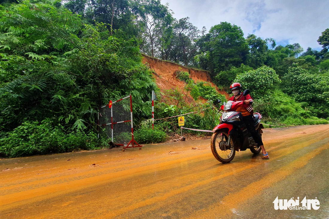 Hàng chục khối đất đá từ đỉnh đồi ta luy dương đổ tràn xuống lấp mương thoát nước ven đường và lòng đường. Mưa tạo thành lớp bùn đỏ, trơn trượt, người đi xe hai bánh qua lại rất khó khăn. Trong ảnh: một phụ nữ phải rà chân để đi qua đoạn đường sạt lở trơn trượt sau cơn mưa