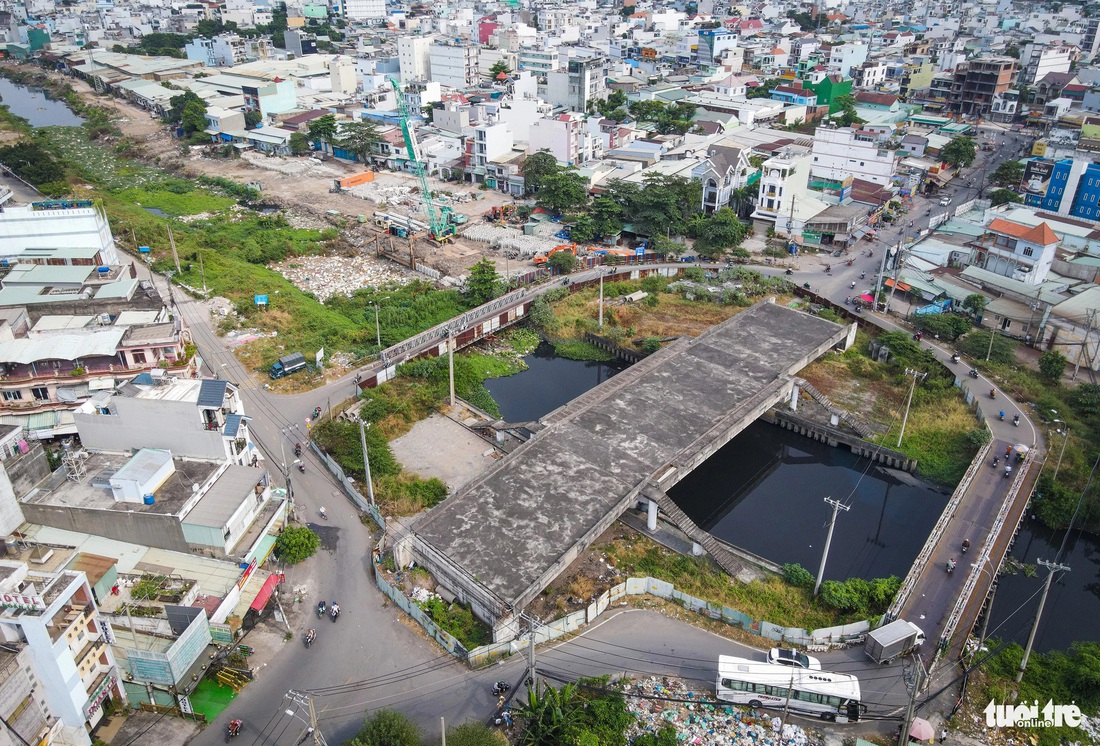 Một tổ xây dựng túc trực tại gói XL5, sát bên là cầu Tân Kỳ - Tân Quý (quận Bình Tân)  bắc qua kênh Tham Lương đang xây dựng dang dở, hai bên là cầu tạm bằng sắt để người dân đi tạm thời - Ảnh: CHÂU TUẤN