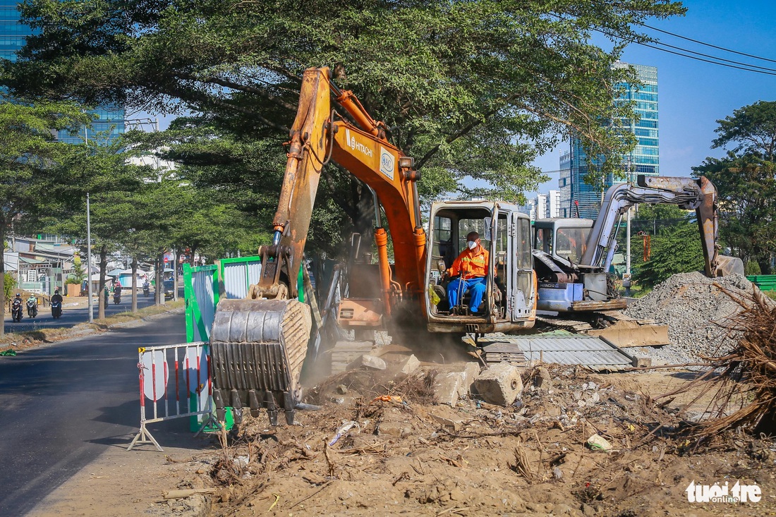 Các công nhân cùng nhiều xe cơ giới đang mở rộng đoạn Nguyễn Văn Linh với khu vực gần cầu Tư Dinh để làm chỗ quay đầu tạm thời cho xe container, xe tải trong thời gian đóng nút giao Nguyễn Văn Linh - Nguyễn Hữu Thọ. Đơn vị thi công đã nhổ tạm 1 cây xanh tại đây và mở rộng nút giao này hơn 20m - Ảnh: CHÂU TUẤN