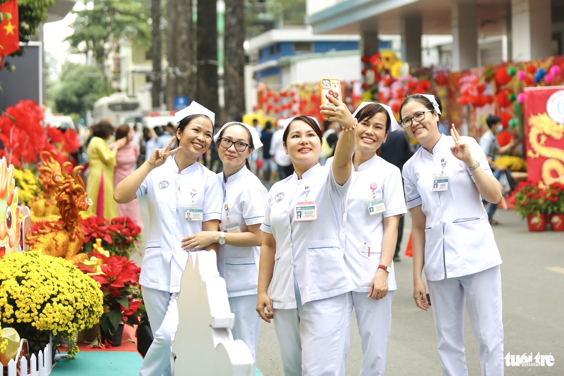 Các điều dưỡng, y tá của bệnh viện tranh thủ ghé đường hoa chụp ảnh lưu niệm trước khi vào ca trực - Ảnh: PHƯƠNG QUYÊN