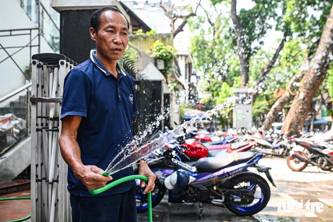 Nam nhân viên bảo vệ này thường xuyên phun nước để hạ nhiệt hơi nóng trên vỉa hè và cho xe cộ đỗ phía ngoài - Ảnh: HỒNG QUANG