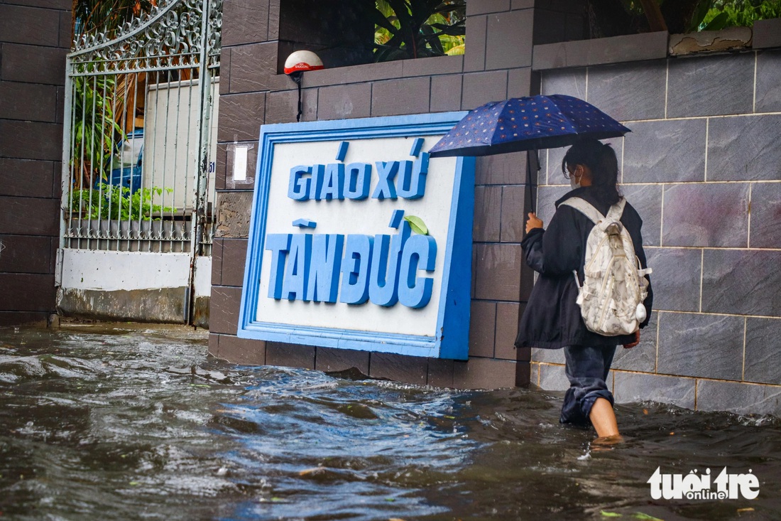 Người đi bộ cố gắng đi sát bên vỉa hè để tránh đoạn ngập sâu trên đường Đỗ Xuân Hợp - Ảnh: CHÂU TUẤN