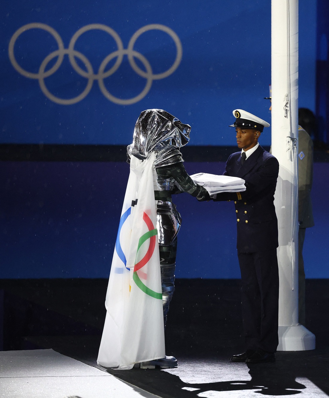 Cờ Olympic được người giấu mặt trao cho đội nghi thức trước lễ thượng cờ - Ảnh: REUTERS