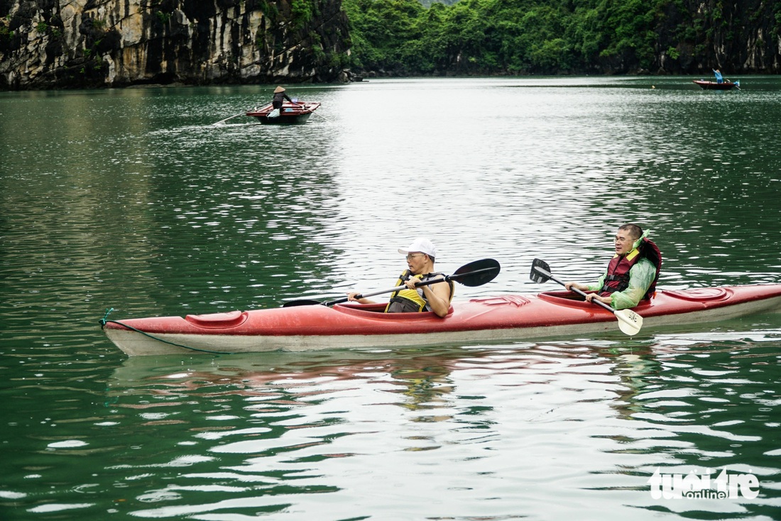 Du khách mặc áo mưa, chèo thuyền kayak khám phá ngôi làng giữa vịnh - Ảnh: NGUYỄN HIỀN