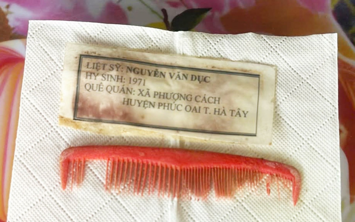 Chiếc lược đỏ và tấm giấy ép plastic trong ngôi mộ in dòng chữ: Liệt sĩ Nguyễn Văn Dục, quê Hà Tây