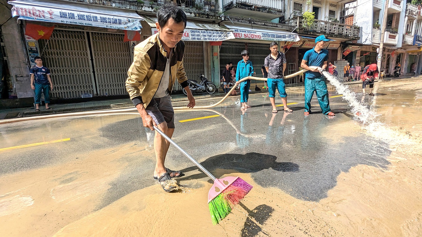 Người dân và lực lượng dân quân dọn bùn non trên đường Huỳnh Thúc Kháng - Ảnh: NHẬT LINH