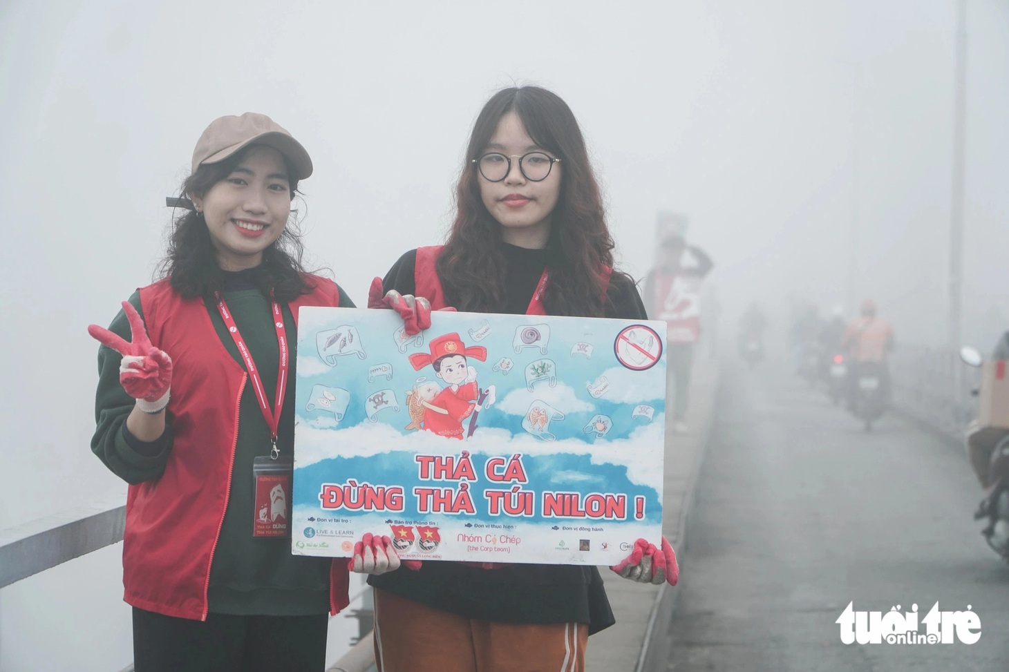 Hai bạn trẻ cầm biển tuyên truyền ngay trên cầu Long Biên trong ngày cúng ông Công, ông Táo - Ảnh: PHẠM TUẤN