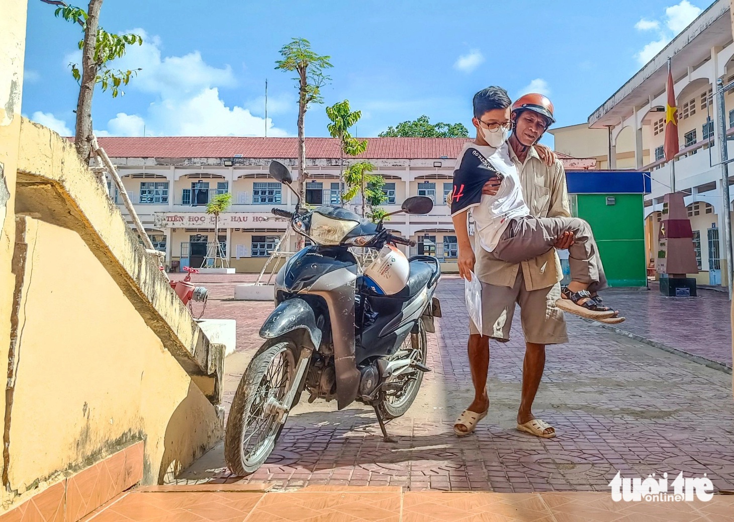 12 năm đồng hành cùng con trai Phạm Quốc Lịnh bị bệnh xương thủy tinh không đi lại được, ông Phạm Văn Út (huyện Cái Nước, tỉnh Cà Mau) bồng con đến lớp để làm thủ tục kỳ thi tốt nghiệp THPT chiều 26-6 - Ảnh THANH HUYỀN