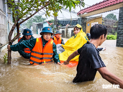 Chính quyền, bộ đội mang xuồng hộ tống dân đi tránh lụt - Ảnh 1. Bộ đội và cán bộ địa phương dầm mưa đưa mẹ con chị Tô Thị Hiếu (32 tuổi), trú kiệt 127 Mẹ Suốt, ra bên ngoài - Ảnh: TẤN LỰC