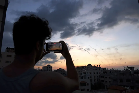 Xung đột Israel - Hamas: Cuộc chiến thông tin - Ảnh 2. Một người đàn ông ghi lại hình ảnh không kích từ Dải Gaza vào Israel ngày 7-10 - Ảnh: AFP