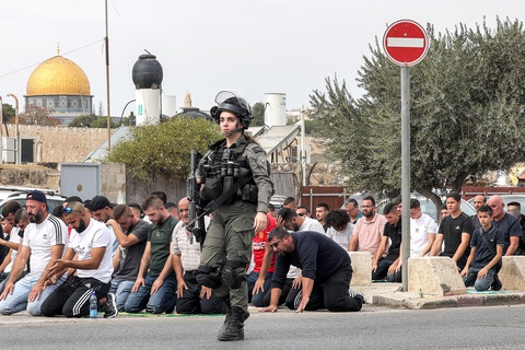 Tin tức thế giới 28-10: Ai Cập dính ‘đạn lạc’; Israel từ chối ngừng bắn ở Gaza - Ảnh 2. Một nữ quân nhân Israel đi ngang qua những tín đồ Hồi giáo đang cầu nguyện ở núi Ô-liu, đông Jerusalem ngày 27-10. Buổi cầu nguyện diễn ra trước các cuộc tuần hành thể hiện tình đoàn kết với người dân Palestine ở Dải Gaza - Ảnh: AFP
