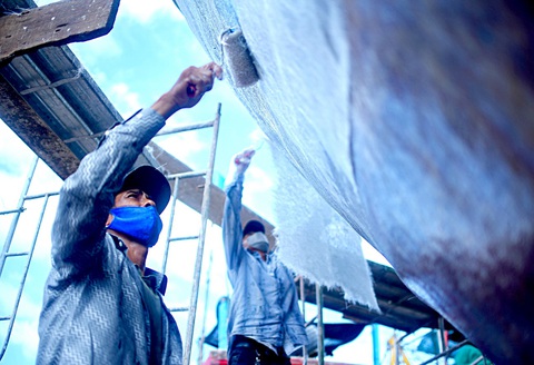 "Bắt bệnh bốc thuốc" cho tàu ra khơi - Ảnh 5. Để tăng độ chống nước vỏ tàu, công nhân phủ lưới nhựa sau đó phủ thêm lớp keo