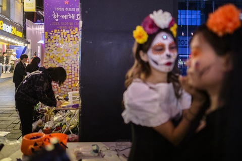 Người dân Hàn Quốc tưởng niệm một năm thảm kịch giẫm đạp Itaewon - Ảnh 6. Ngày 28-10, người qua đường viết lưu bút tưởng niệm các nạn nhân lên giấy ghi chú và dán lên mảnh tường ở hẻm Itaewon (trái), trong khi những người khác đang hóa trang tham gia lễ hội Halloween (phải) - Ảnh: AFP