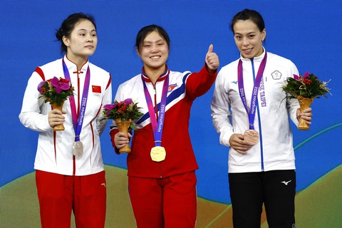Trong lần đầu thi đấu quốc tế, Kim Ilgyong (giữa) ở tuổi 20 đã đánh bại kỷ lục gia thế giới Kuo Hsing Chun (bìa phải) - Ảnh: REUTERS Trong lần đầu thi đấu quốc tế, Kim Ilgyong (giữa) ở tuổi 20 đã đánh bại kỷ lục gia thế giới Kuo Hsing Chun (bìa phải) - Ảnh: REUTERS