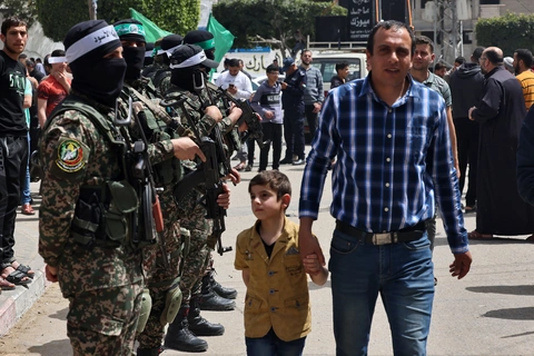 Một người đàn ông Palestine cùng con trai đi ngang qua các thành viên của Hamas ở thành phố Jabalia, phía Bắc dải Gaza, ngày 7-4 - Ảnh: AFP Một người đàn ông Palestine cùng con trai đi ngang qua các thành viên của Hamas ở thành phố Jabalia, phía Bắc dải Gaza, ngày 7-4 - Ảnh: AFP