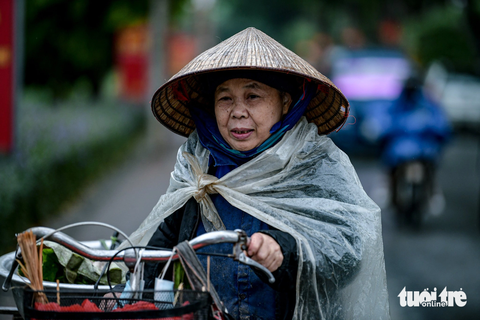 Người Hà Nội co ro trong gió lạnh đầu mùa - Ảnh 6. Cắt rau để đi bán từ sáng sớm, bà Tý (70 tuổi) cho biết hôm nay phải mặc ấm hơn. Ngoài áo, bà còn mặc 2 áo mưa để tránh mưa và lạnh - Ảnh: NAM TRẦN