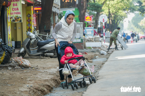 'Đến hẹn lại lên', cuối năm, loạt vỉa hè ở Hà Nội lại bị xới tung để... lát lại - Ảnh 3. Một người dân loay hoay đẩy chiếc xe chở em bé đi qua vỉa hè bị đào xới lồi lõm - Ảnh: PHẠM TUẤN