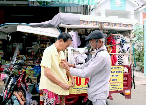 Ông Tư Ẩn giúp một người ướm thử chiếc áo mới ngay tại gian hàng 0 đồng Ông Tư Ẩn giúp một người ướm thử chiếc áo mới ngay tại gian hàng 0 đồng