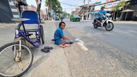 Công ty xổ số lãi kỷ lục, người bán vé số phải xuống đường năn nỉ người mua- Ảnh 1. Ông Nguyễn Văn Vinh (52 tuổi, ngụ huyện Châu Thành, tỉnh Tiền Giang) phải ngồi dưới lòng đường mong bán hết vé số - Ảnh: MẬU TRƯỜNG