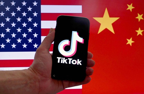 Làn sóng cấm TikTok lan rộng - Ảnh 1. Ảnh minh họa của Hãng tin AFP cho thấy logo của TikTok hiển thị trên màn hình điện thoại iPhone phía trước cờ Mỹ và Trung Quốc - Ảnh: AFP