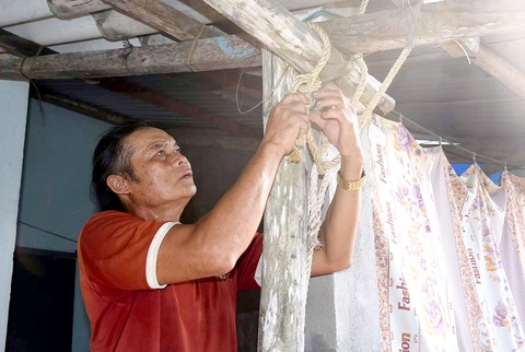 Ông Anh cột lại mái nhà của mình đề phòng gió lốc - Ảnh: TRẦN MAI Ông Anh cột lại mái nhà của mình đề phòng gió lốc - Ảnh: TRẦN MAI