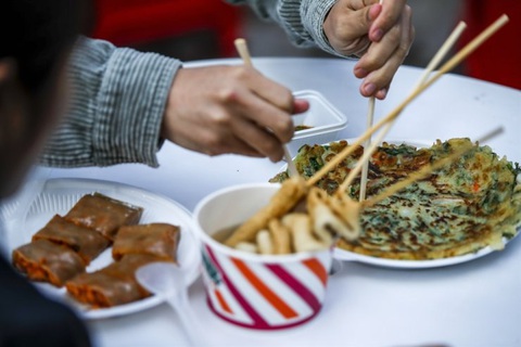 Du khách thử món bánh kếp hành lá hải sản và chả cá trong nước dùng cá mòi tại một lễ hội ẩm thực khu vực được tổ chức ở Quận Mapo của Seoul năm 2022 - Ảnh: Korea Times Du khách thử món bánh kếp hành hải sản và chả cá trong nước dùng cá mòi tại một lễ hội ẩm thực khu vực được tổ chức ở Quận Mapo của Seoul năm 2022 - Ảnh: Korea Times