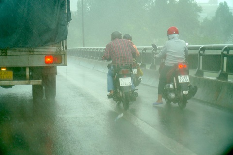Người đi xe máy bị gió quật nghiêng ngả khi qua cầu Rạch Miễu - Ảnh 3. Một số người đi xe máy qua cầu Rạch Miễu gặp lúc mưa phải nép vào xe tải để tránh bị gió quật - Ảnh: MẬU TRƯỜNG