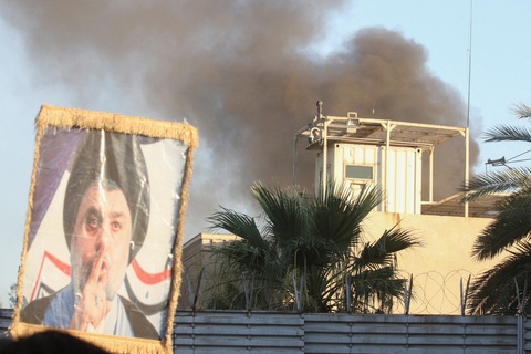 Người biểu tình Iraq trèo tường, phóng hỏa đại sứ quán Thụy Điển - Ảnh 1. Một người biểu tình giơ cao chân dung giáo sĩ Moqtada al-Sadr khi khói bốc lên từ tòa nhà Đại sứ quán Thụy Điển trong một cuộc biểu tình gần đại sứ quán, vài giờ sau khi họ xông vào và phóng hỏa Đại sứ quán Thụy Điển sáng 20-7 - Ảnh: REUTERS