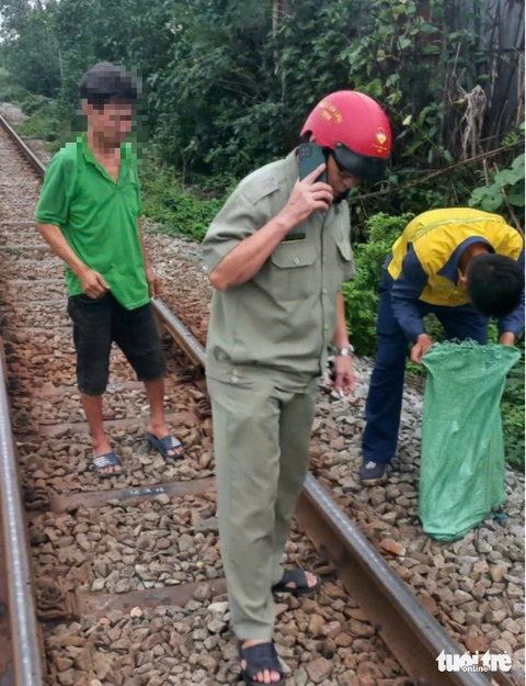 Người dân bắt trộm tháo đường ray: ‘Tôi làm vì biết mất một con ốc sẽ uy hiếp chạy tàu - Ảnh 1. Người đàn ông (mặc áo xanh, đứng bên trái) tháo trộm ốc, vật tư trên đường ray - Ảnh: CTV