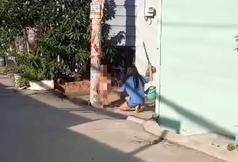 Bé trai 8 tuổi bị một phụ nữ trói vào cột điện đánh bằng chổi - Ảnh 1. Người phụ nữ dùng chổi đánh bé trai trần truồng đang bị trói vào cột điện - Ảnh cắt từ video do người dân ghi lại