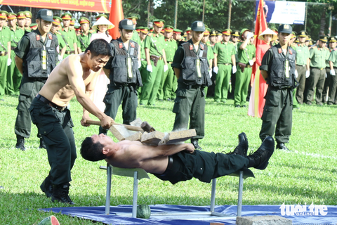 Chiến sĩ công an biểu diễn bài nằm trên hai lưỡi đao, đặt tảng đá lên bụng rồi đồng đội dùng búa đập bể tảng đá - Ảnh: KHẮC HIẾU