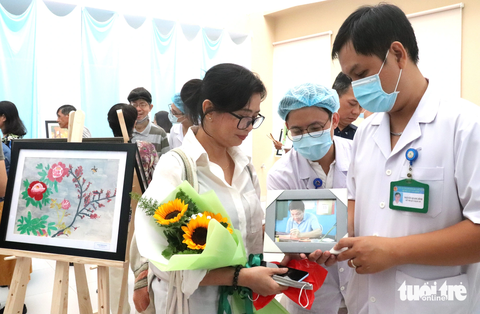 Triển lãm tranh bệnh nhân: Người vợ xúc động ngắm ảnh của người chồng đã qua đời - Ảnh 2. Bệnh viện An Bình bất ngờ tặng chị Đoàn Nguyên Thùy bức ảnh chụp anh Phạm Minh Đức (chồng chị Thùy) đang vẽ tranh bằng tay trái lúc còn sống - Ảnh: XUÂN MAI