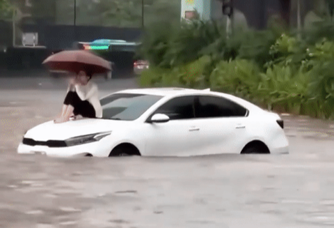 Đường Hà Nội ngập sâu, nữ tài xế ngồi trên nóc ô tô chờ cứu hộ - Ảnh 1. Cảnh chị C. ngồi trên nóc ô tô giữa đường ngập nước được người đi đường ghi lại - Ảnh: Mạng xã hội