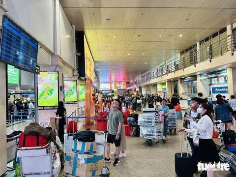 Sân bay Tân Sơn Nhất đông khách hơn nhưng vẫn ổn- Ảnh 5. Sân bay đông, đi lại vẫn thông thoáng. Hành khách theo dõi màn hình hiển thị thông tin chuyến bay - Ảnh: CÔNG TRUNG