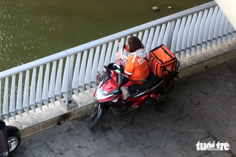 Nữ shipper ăn cơm trưa đưới dạ cầu tránh nắng - Ảnh: T.T.D. Nữ shipper tranh thủ ăn cơm trưa dưới dạ cầu tránh nắng