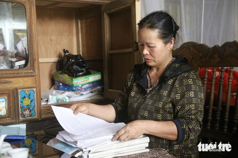 Sau 7 năm được minh oan, cựu tử tù Hàn Đức Long vẫn chờ bồi thường- Ảnh 2. Bà Nguyễn Thị Mai (vợ ông Hàn Đức Long) xem lại những lá đơn bà từng viết để gửi đến các cơ quan chức năng, kêu oan cho chồng - Ảnh: DANH TRỌNG