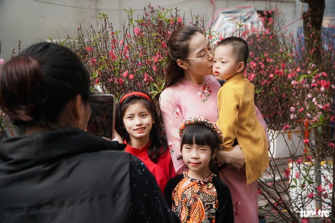 Người Hà Nội đi sắm Tết ngày nắng ấm, phố cổ, trung tâm thương mại kín người- Ảnh 2. 4 mẹ con cùng nhau chụp ảnh với cây đào trên phố cổ - Ảnh: PHẠM TUẤN