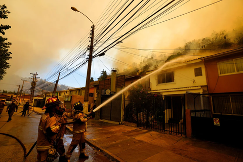 Firefighters protectively spray water on homes as forest fires burn nearby. Esteban Felix/AP Lính cứu hỏa phun nước bảo vệ các ngôi nhà khi đám cháy rừng bùng phát gần đó - Ảnh: Esteban Felix/AP