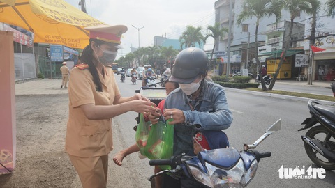 Lập 'trạm dừng chân nghĩa tình' phát nước, sữa cho bà con trên đường về quê- Ảnh 1. Lực lượng cánh sát giao thông Công an tỉnh An Giang phát nước suối và sữa cho 4 mẹ con chị Nhung - Ảnh: BỬU ĐẤU