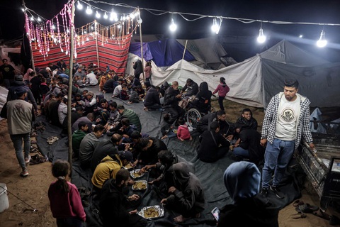 Hàng triệu tín đồ Hồi giáo bước vào tháng Ramadan, chia sẻ nỗi đau với người Gaza- Ảnh 7. Những người Palestine đang ăn bữa Iftar tại một trại tị nạn dành cho người di tản ở thành phố Rafah, miền nam Dải Gaza tối 11-3 - Ảnh: AFP
